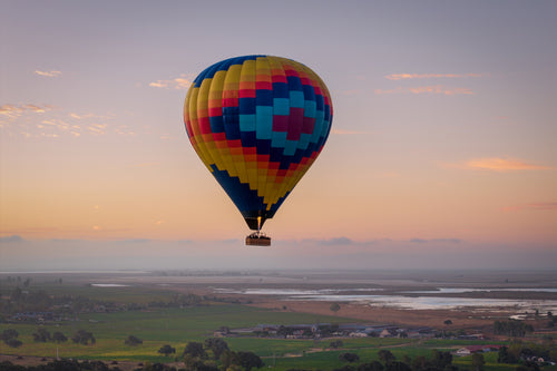Carried by Light, a colorful hot air balloon floating above the Sonoma Valley beneath a soft pink and lavender sunrise sky.
