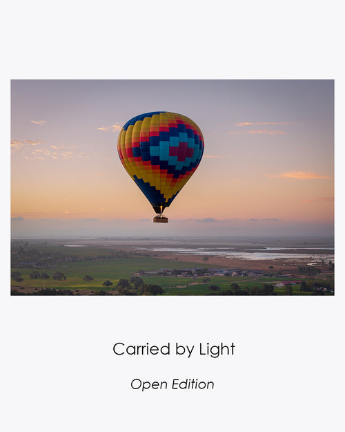 Collection card for Carried by Light, an open-edition photograph of a colorful hot air balloon floating above the Sonoma landscape at sunrise.
