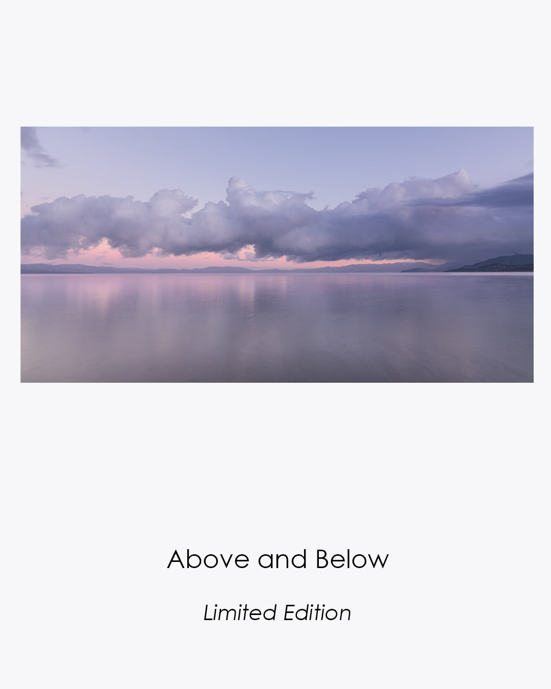 Lake Tahoe at sunrise after snowfall, with clouds gathered above still water reflecting the soft pink dawn light.