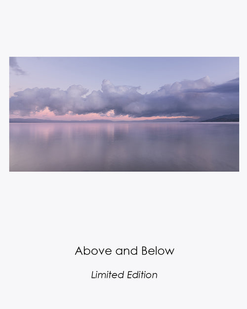 Lake Tahoe at sunrise after snowfall, with clouds gathered above still water reflecting the soft pink dawn light.