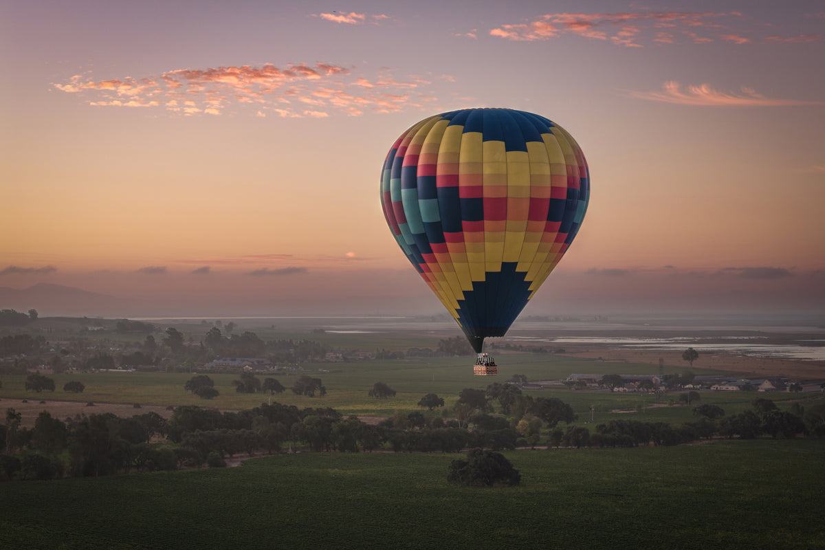 Aerial view of a colorful hot-air balloon floating above Sonoma vineyards and morning mist beneath pink-and-gold clouds.