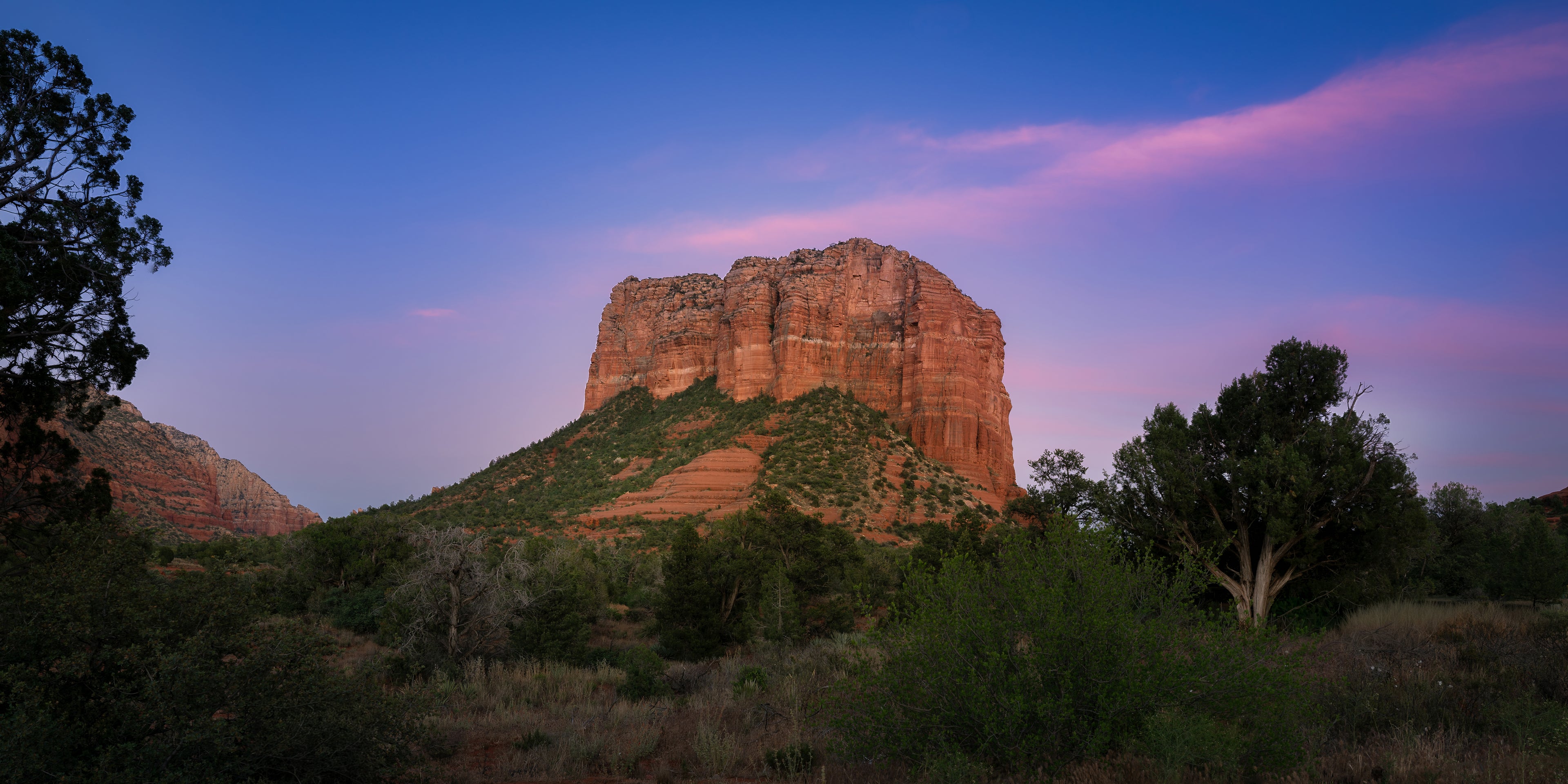 Panoramic photograph of Courthouse Butte beneath a sweeping rose-and-lavender cloud as the Sedona landscape settles into dusk.