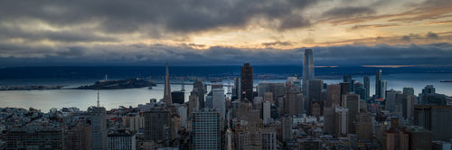 Gathering Light, a panoramic aerial photograph of San Francisco as dawn breaks through layered clouds above the skyline and Bay.