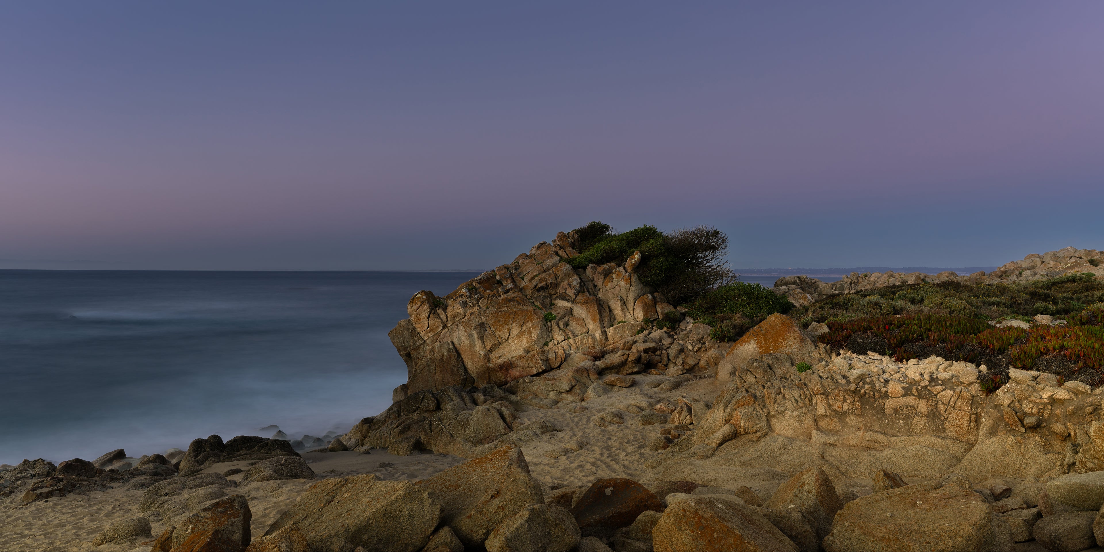 Lavender blue-hour light settling over the water as the last warmth of day lingers across the coastal rocks.
