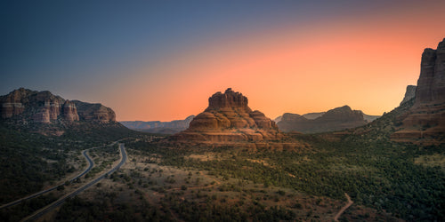 Bell Rock rising above the winding desert road as the first warm light of morning fills the Sedona sky.