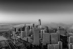 Black-and-white aerial photograph of the San Francisco skyline emerging through layers of fog.