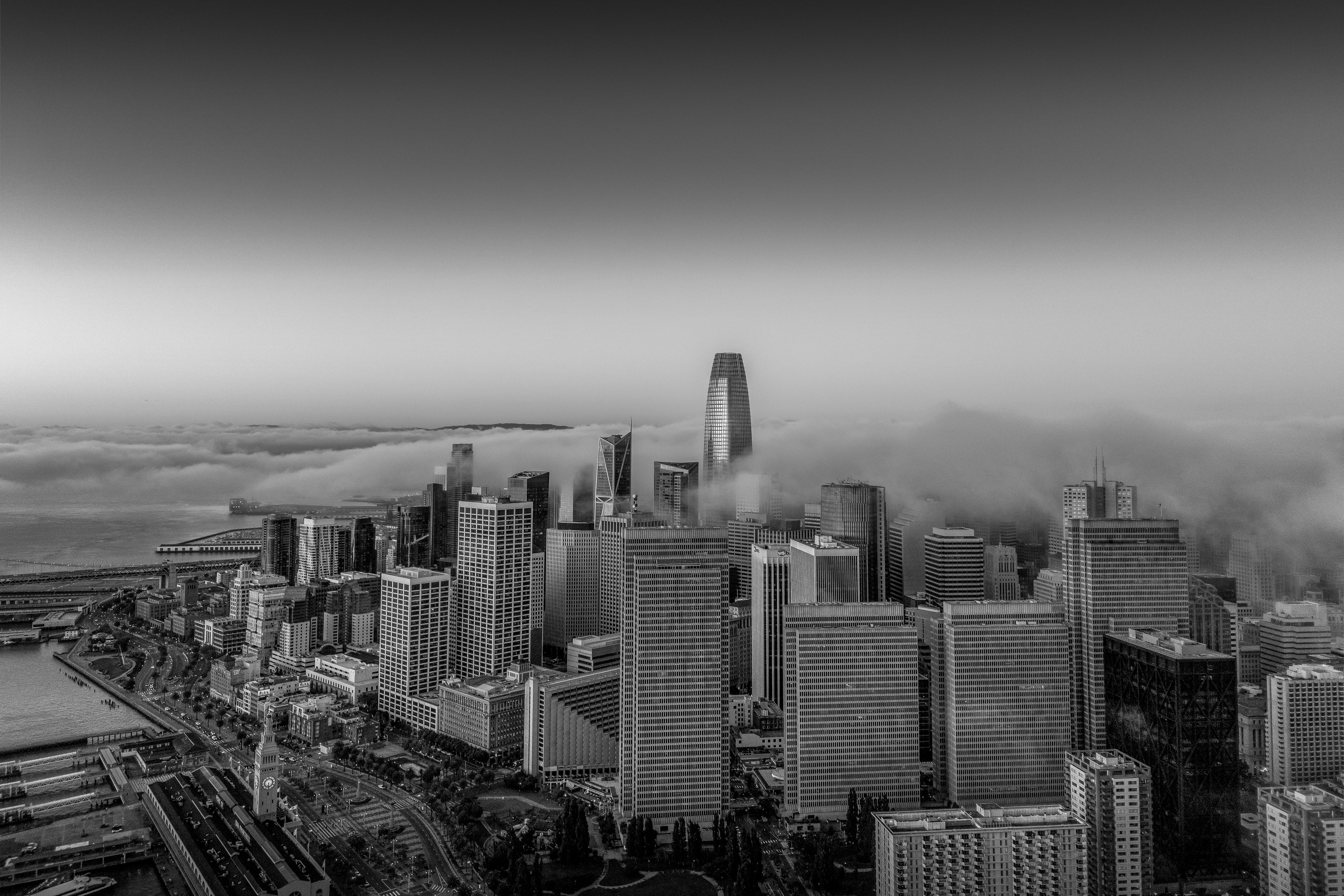 Black-and-white aerial photograph of the San Francisco skyline emerging through layers of fog.