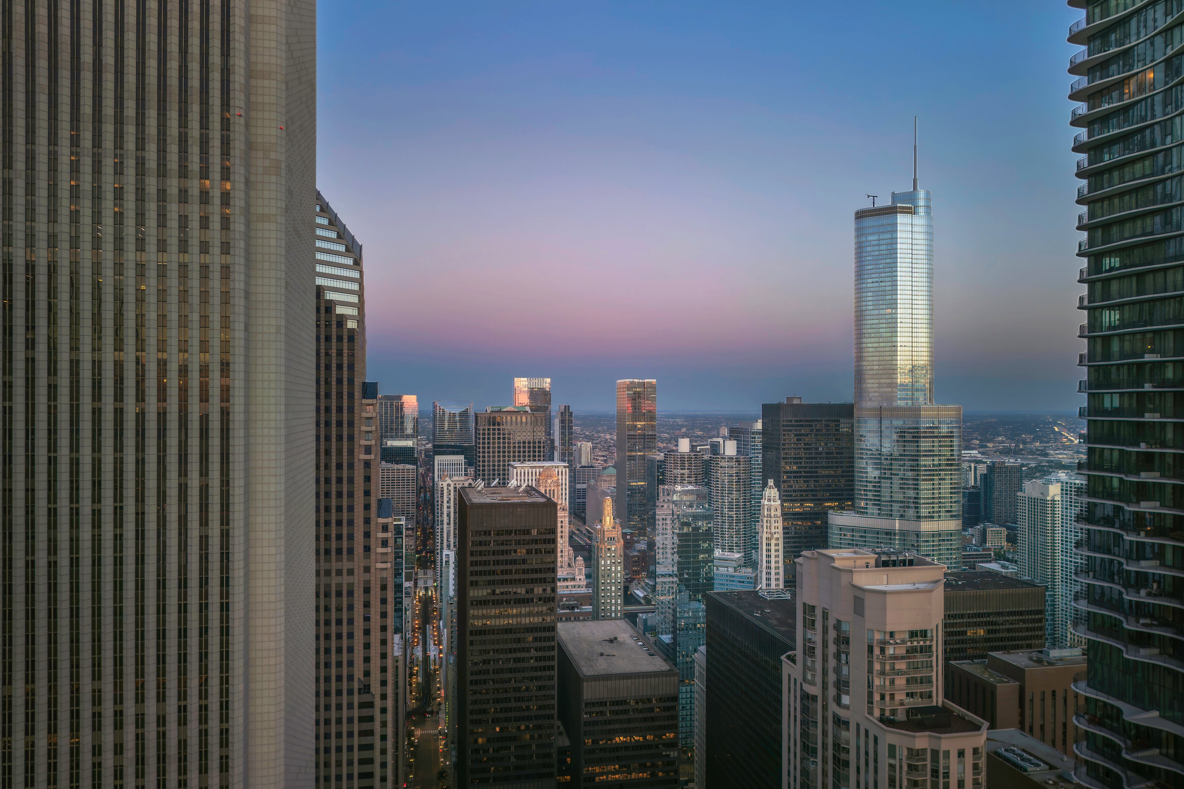 Aerial view of the Chicago skyline at sunrise, photographed by drone between two towering buildings beneath a blue, lavender, and rose sky.