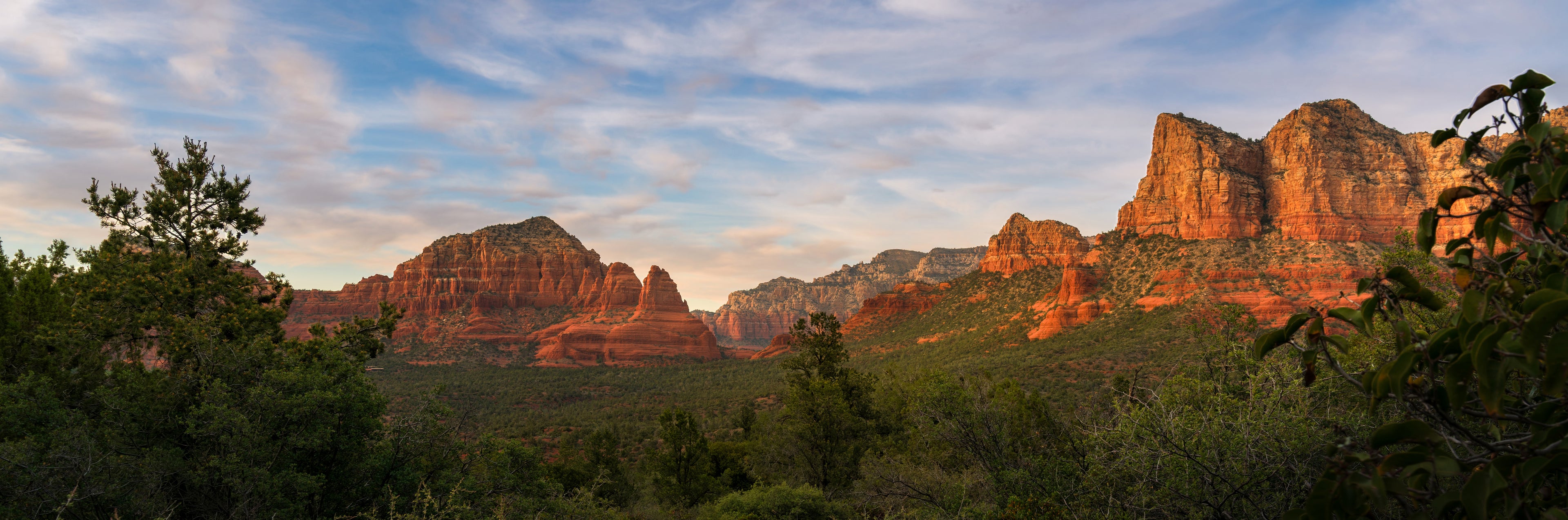 Panoramic photograph of Sedona’s red rock formations illuminated by warm evening light above the forested valley.
