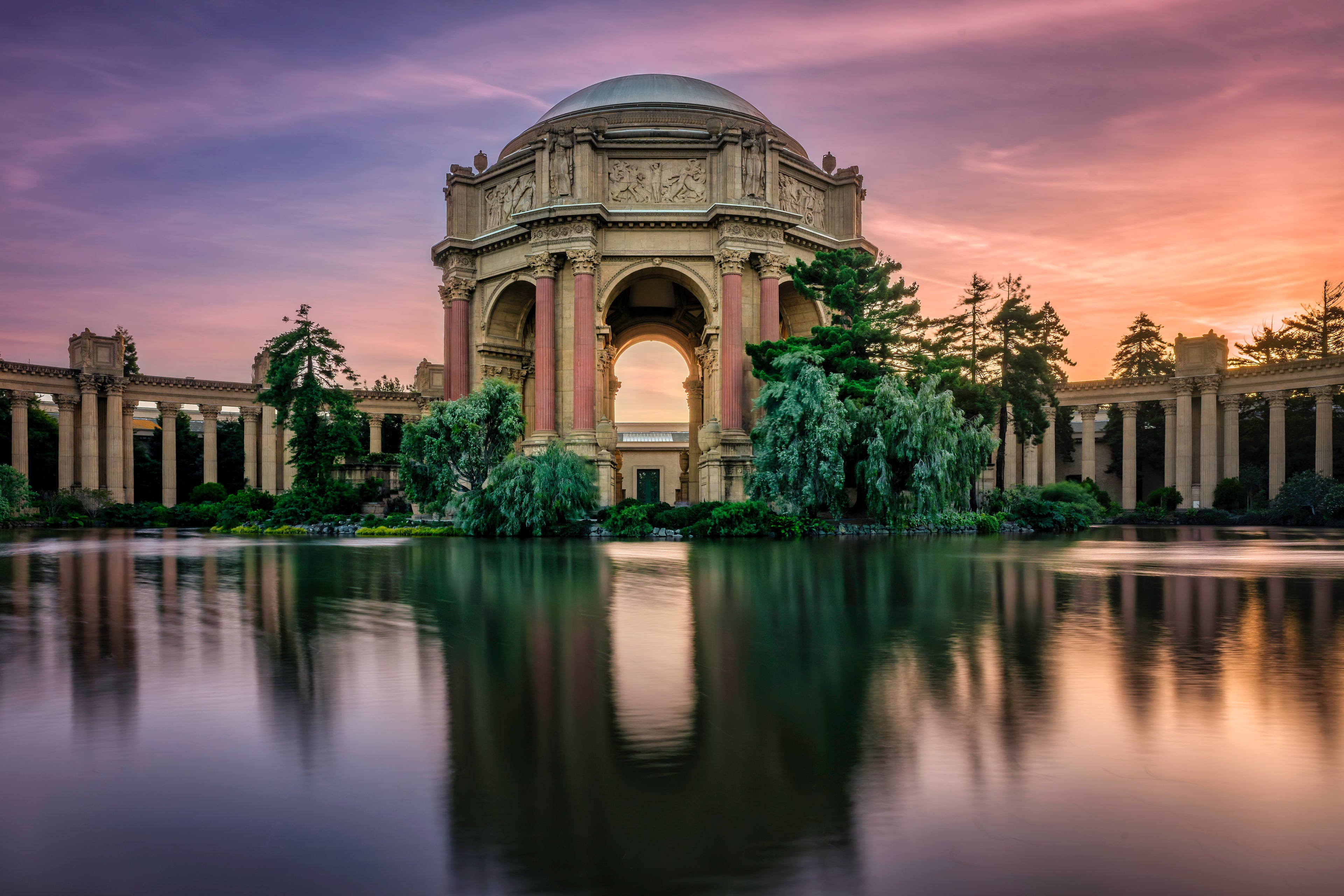 The Palace of Fine Arts reflected in still water beneath a glowing pink and lavender sunset in San Francisco.