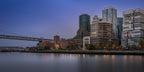 Panoramic view of San Francisco’s Embarcadero at dawn, with the Bay Bridge, Hills Bros. building, Cupid’s Span, and city skyline beneath lifting fog as warm lights reflect across the bay.