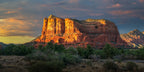 Panoramic photograph of Courthouse Butte illuminated by brilliant sunset light beneath dark blue-gray clouds in Sedona, Arizona.