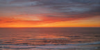 Brilliant orange and coral sunset clouds reflected across rhythmic ocean waves approaching the shore.