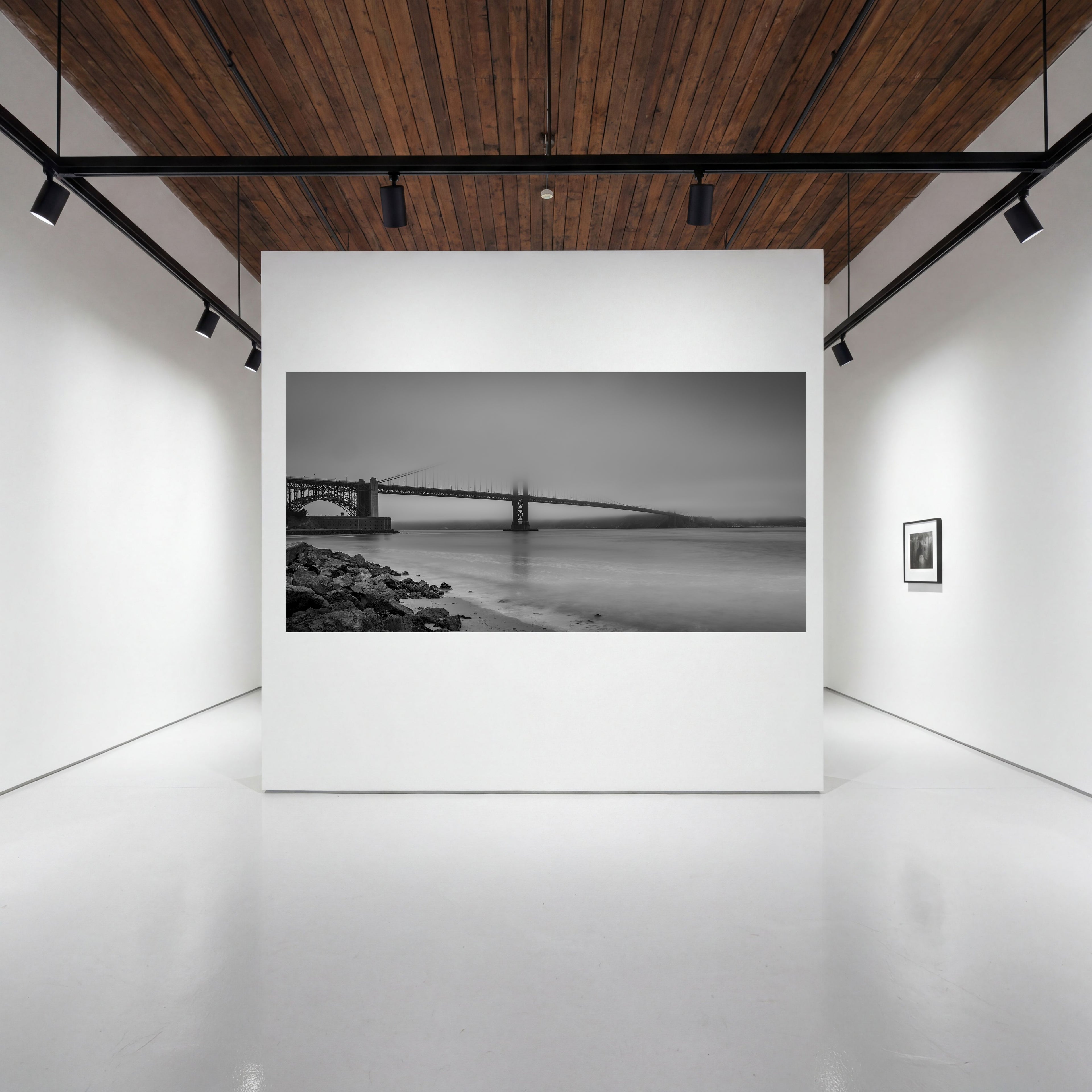 Large panoramic print of Where Certainty Ends, showing the Golden Gate Bridge fading into fog, displayed on a white wall in a contemporary gallery.